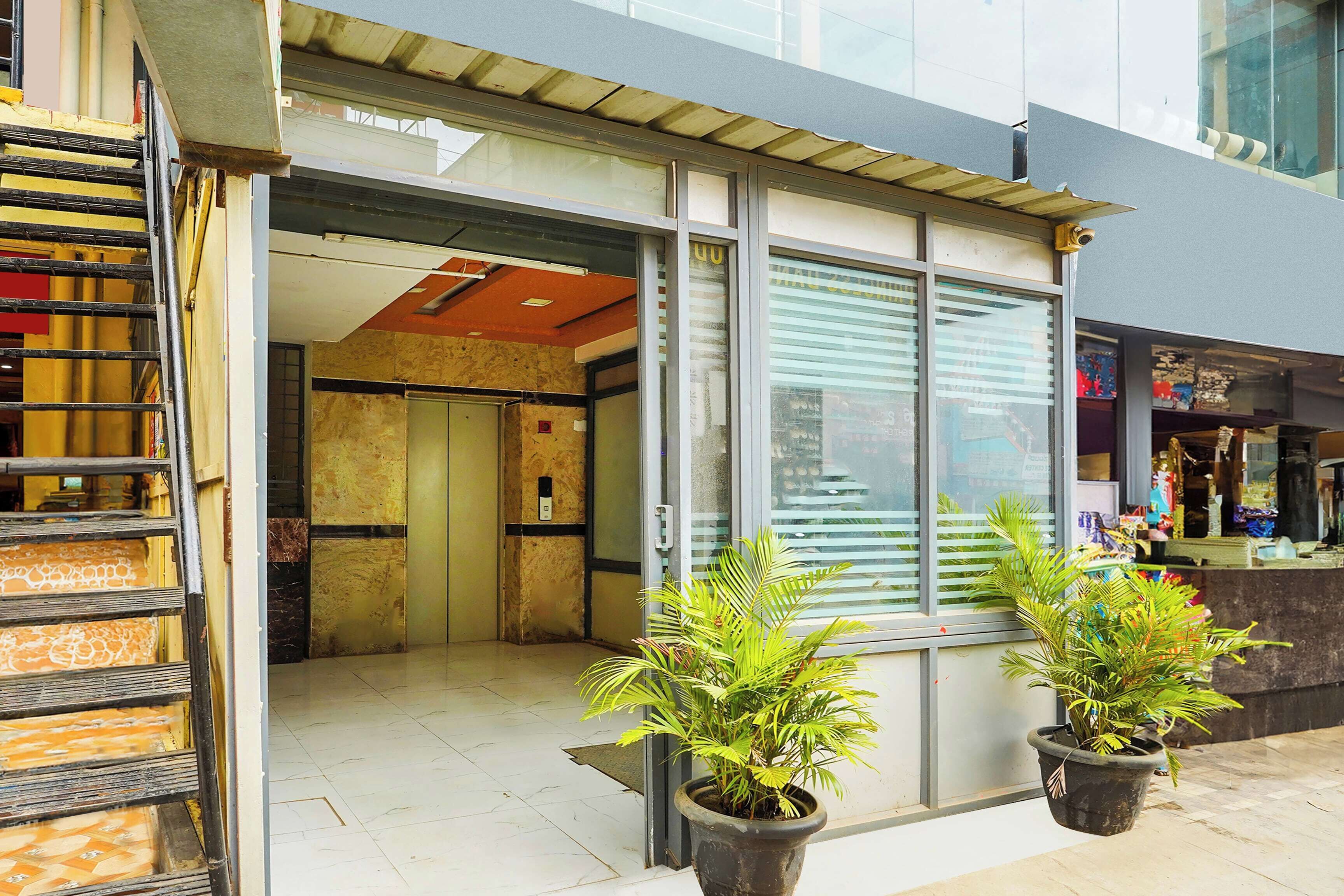 A building entrance with a glass door, a metal staircase, and potted plants.