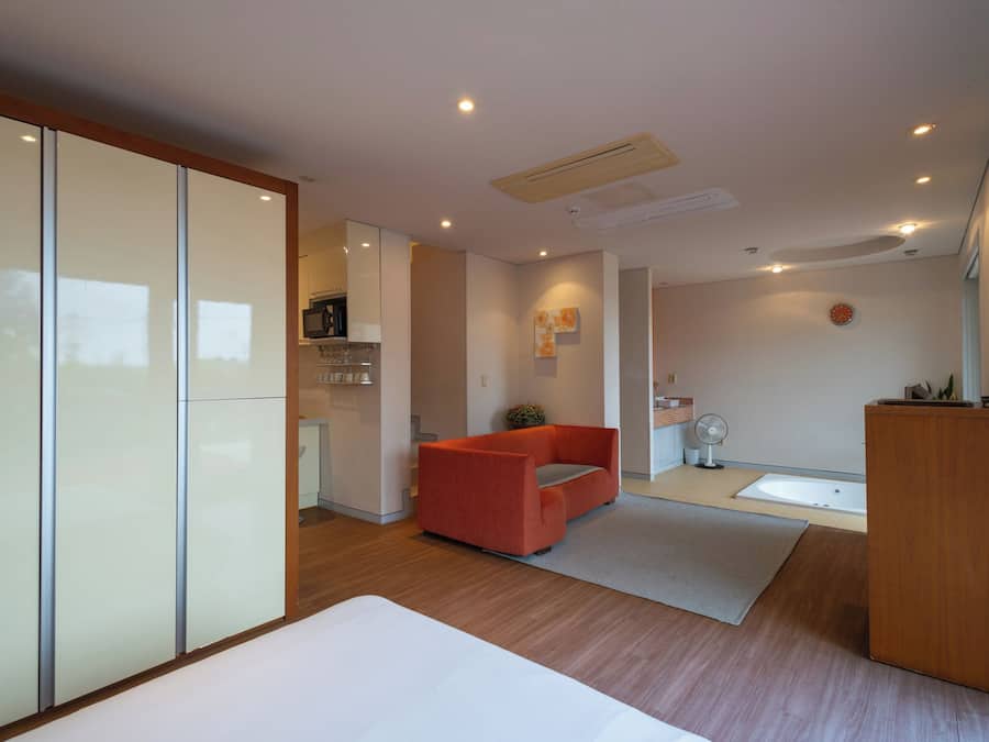 Una habitación de hotel moderna con cama, un sofá rojo, una pequeña cocina y un baño.