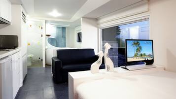 A hotel room with a bed, a desk, a television, a chair, a kitchenette, and a bathroom.