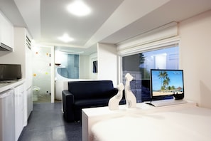 A hotel room with a bed, a desk, a television, a chair, a kitchenette, and a bathroom.