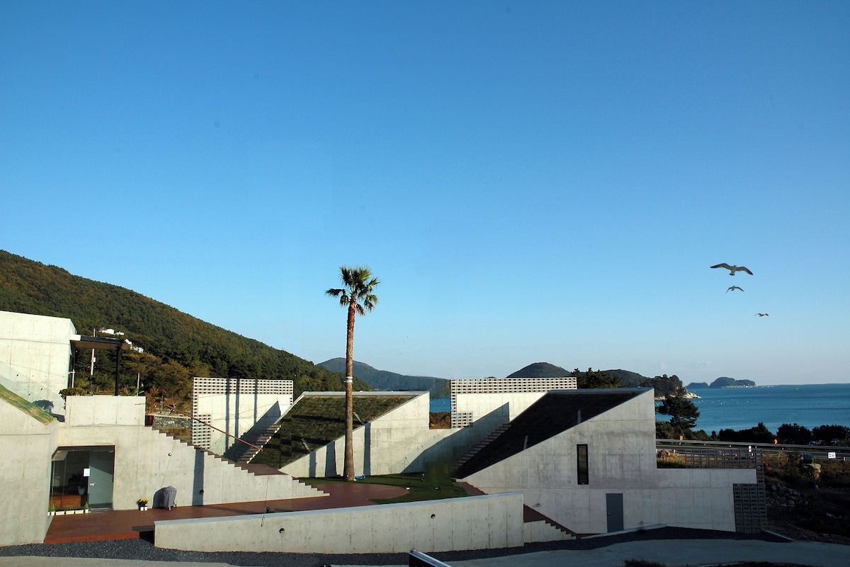 A modern building with a staircase leading to a terrace overlooking a body of water.