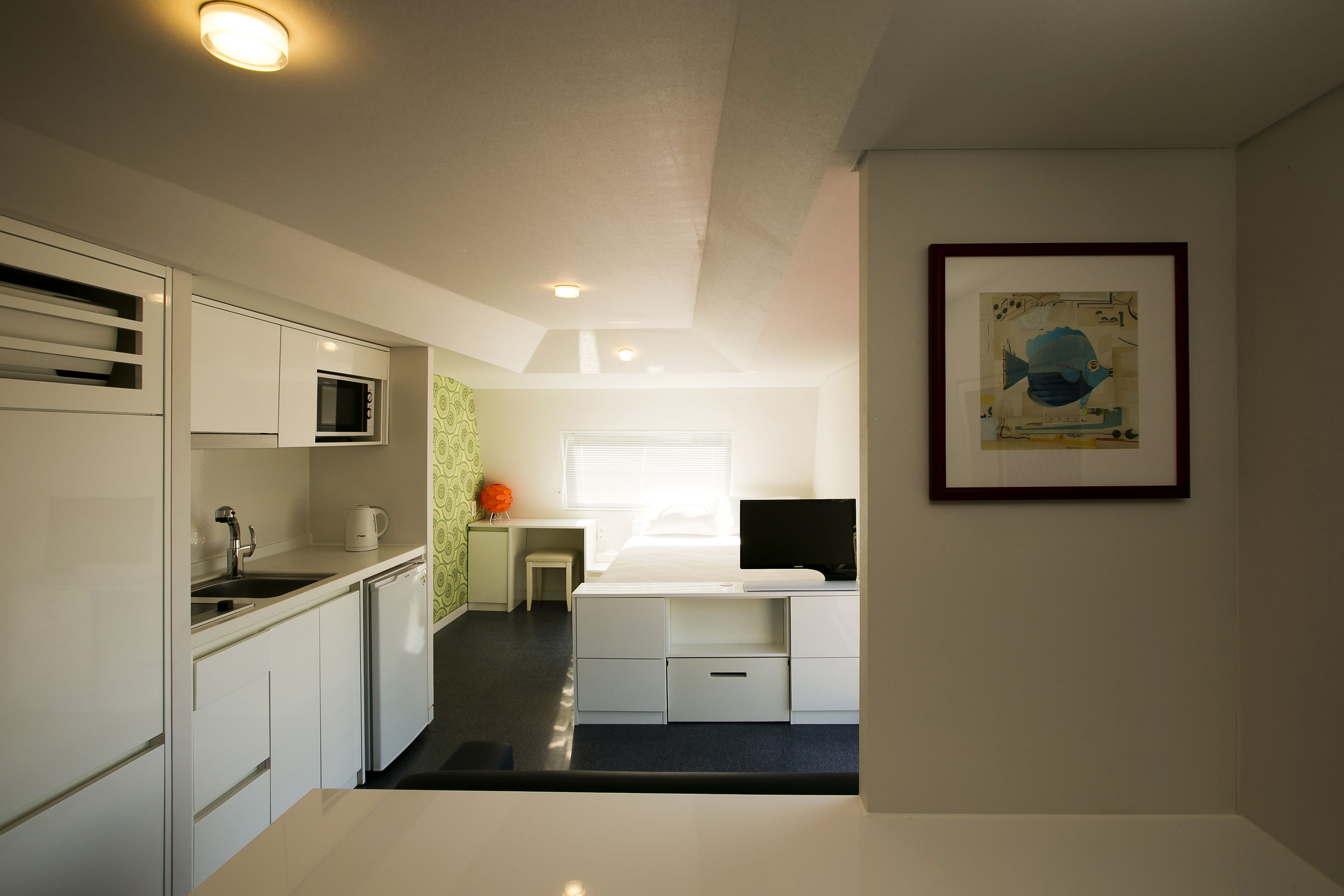 Una cocina compacta con electrodomésticos modernos, un comedor con mesa y sillas, y una obra de arte enmarcada en la pared.