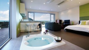 Habitación de hotel moderna con un ventanal grande, jacuzzi, sofá, televisor y cama.