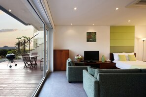 Una habitación de hotel moderna con un ventanal grande, un sofá, un televisor y una cama.