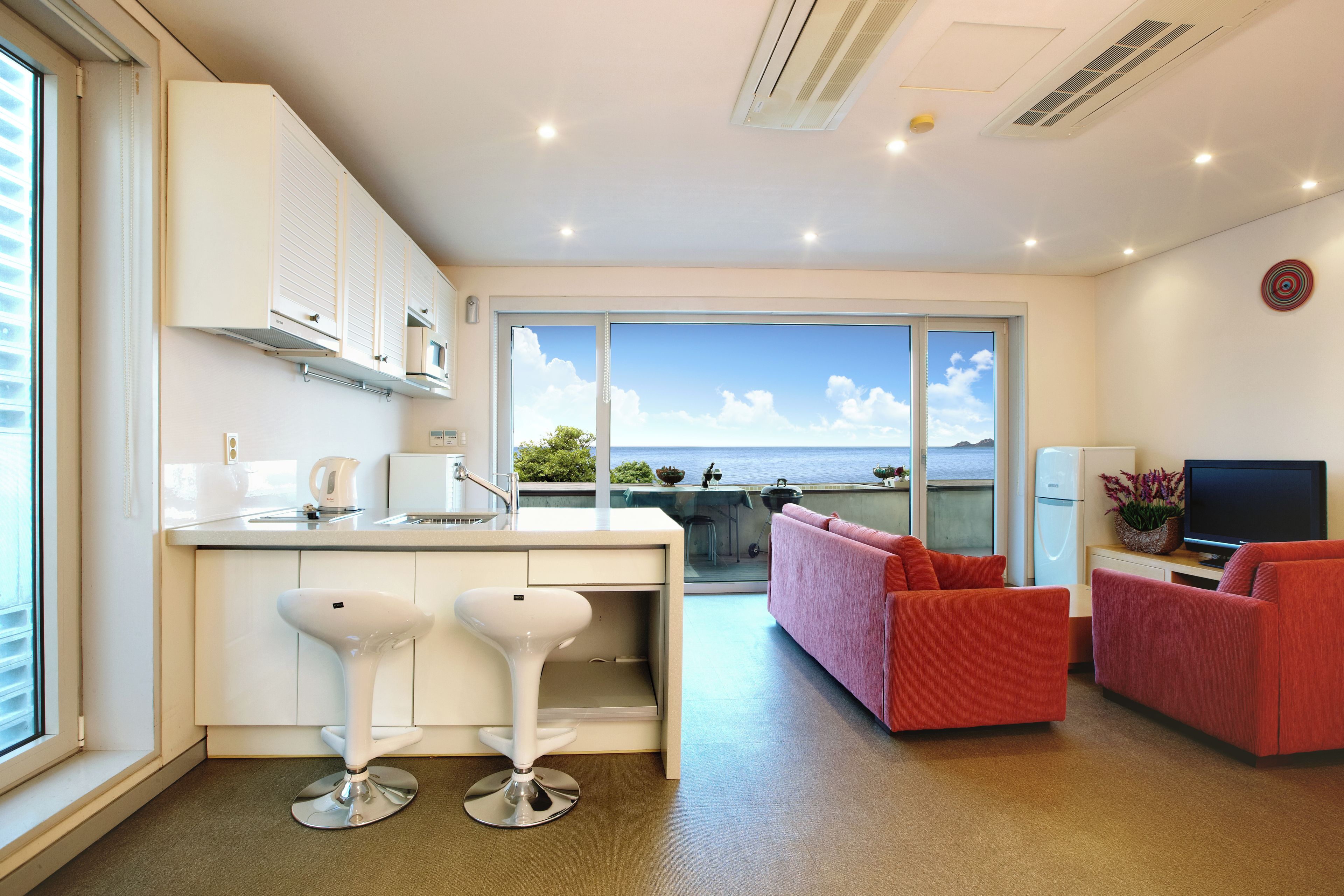 Una cocina moderna con un ventanal grande, una zona de comedor con un sofá rojo y un televisor.