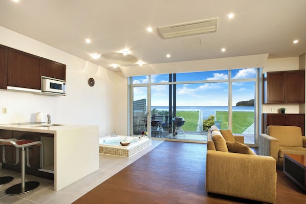Una cocina moderna con microondas integrado, una zona de comedor con taburete de bar, un amplio ventanal con vista al mar y un rincón de estar acogedor con sofá y sillón.