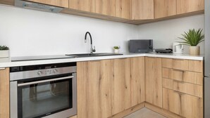 Eine moderne Küche mit Holzschränken, einem Edelstahlbackofen, einer Spüle und einer kleinen Arbeitsplatte mit Pflanze und Wasserkocher.