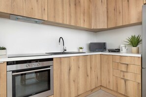 A modern kitchen with wooden cabinets, a stainless steel oven, a sink, and a small countertop with a plant and a kettle. - Spacious Apartment with a Balcony | Parking | 2 Bedrooms (Katowice)