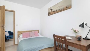 Ein Schlafzimmer mit einem Bett, einem Schreibtisch, einem Stuhl, einer Lampe und einem Bild an der Wand.