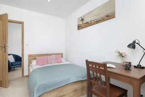 A bedroom with a bed, a desk, a chair, a lamp, and a painting on the wall. - Spacious Apartment with a Balcony | Parking | 2 Bedrooms (Katowice)