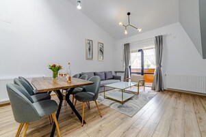 A modern living room with a dining area, a sofa set, and a large window with curtains.