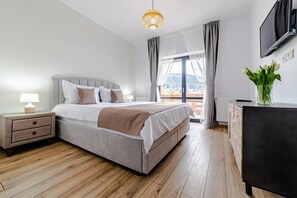 Un dormitorio con cama, mesita de noche, lámpara, cómoda, televisor y ventana con cortinas.