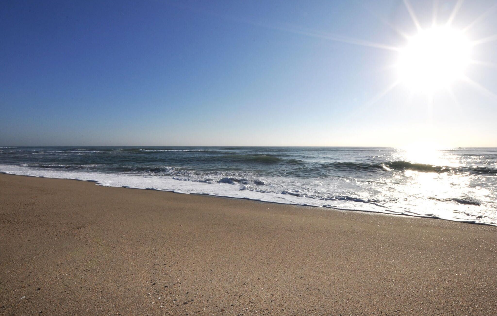Une plage avec des vagues, un ciel dégagé et un soleil éclatant.