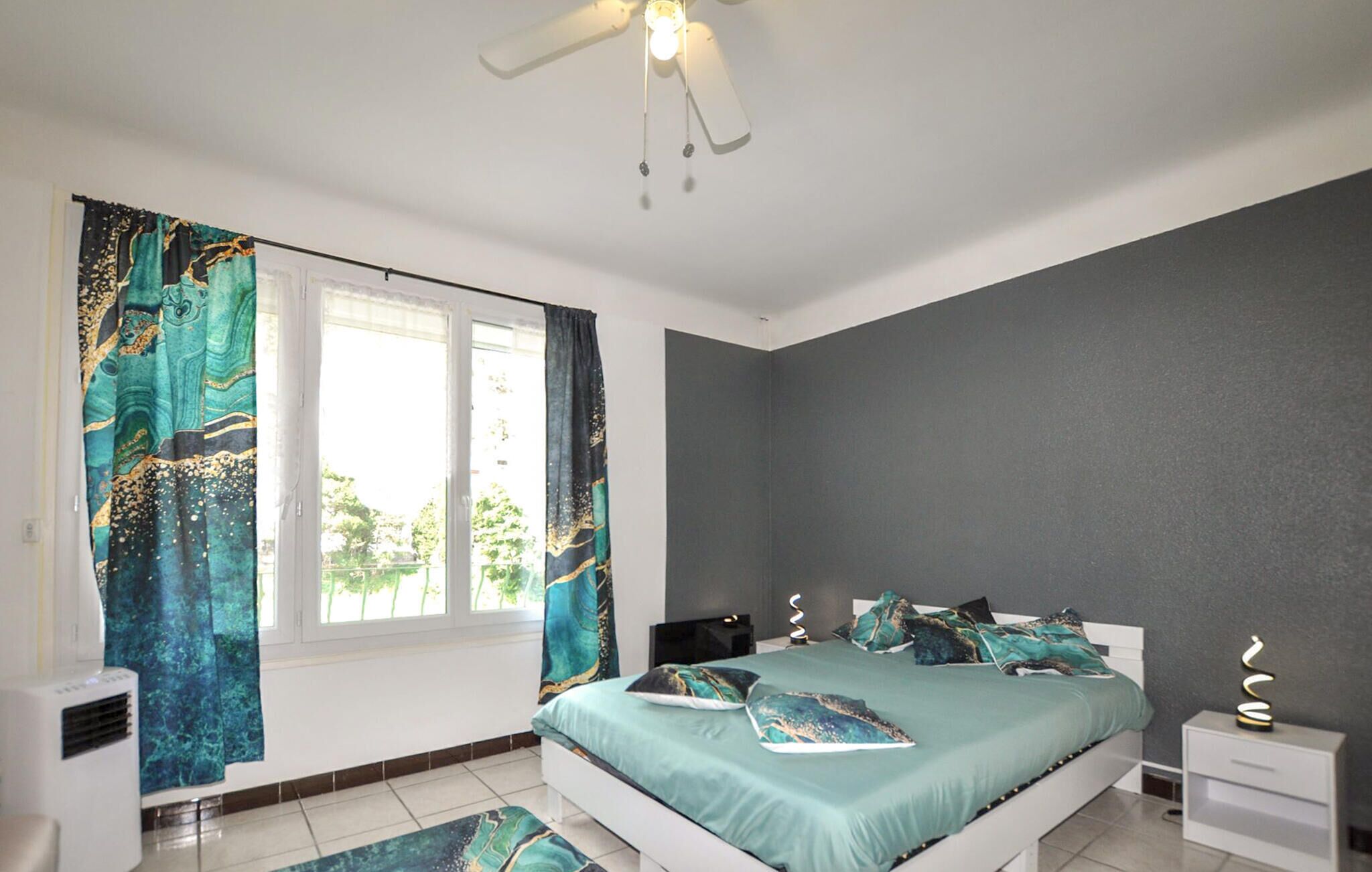 A bedroom with a bed, curtains, a ceiling fan, and a nightstand.