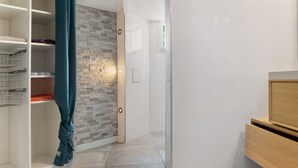 A hallway with a tiled floor, a wardrobe with metal shelves, a wall with a stone-like pattern, and a door with a light switch. - Apartment 'Villa Andalouse' with Private Terrace, Wi-Fi and Air Conditioning (Poussan)