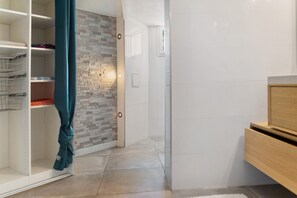 Ein Flur mit Fliesenboden, einem Schrank mit Metallregalen, einer Wand mit Steinoptik und einer Tür mit Lichtschalter.