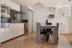 Eine moderne Küche mit integrierten Geräten, ein Essbereich mit Tisch und Stühlen sowie eine hängende Leuchte.