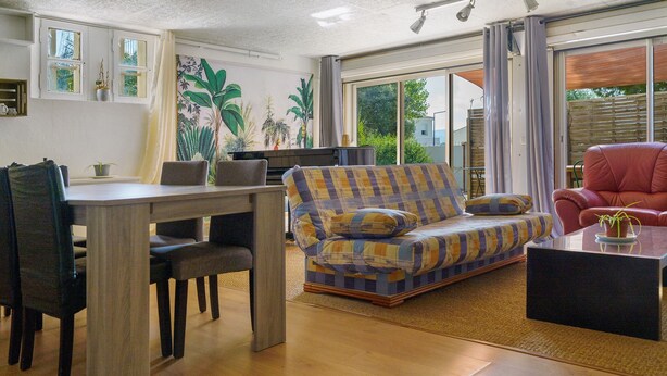 A living room with a sofa, a dining table with chairs, and a red armchair. - Apartment 'Villa Andalouse' with Private Terrace, Wi-Fi and Air Conditioning (Poussan)