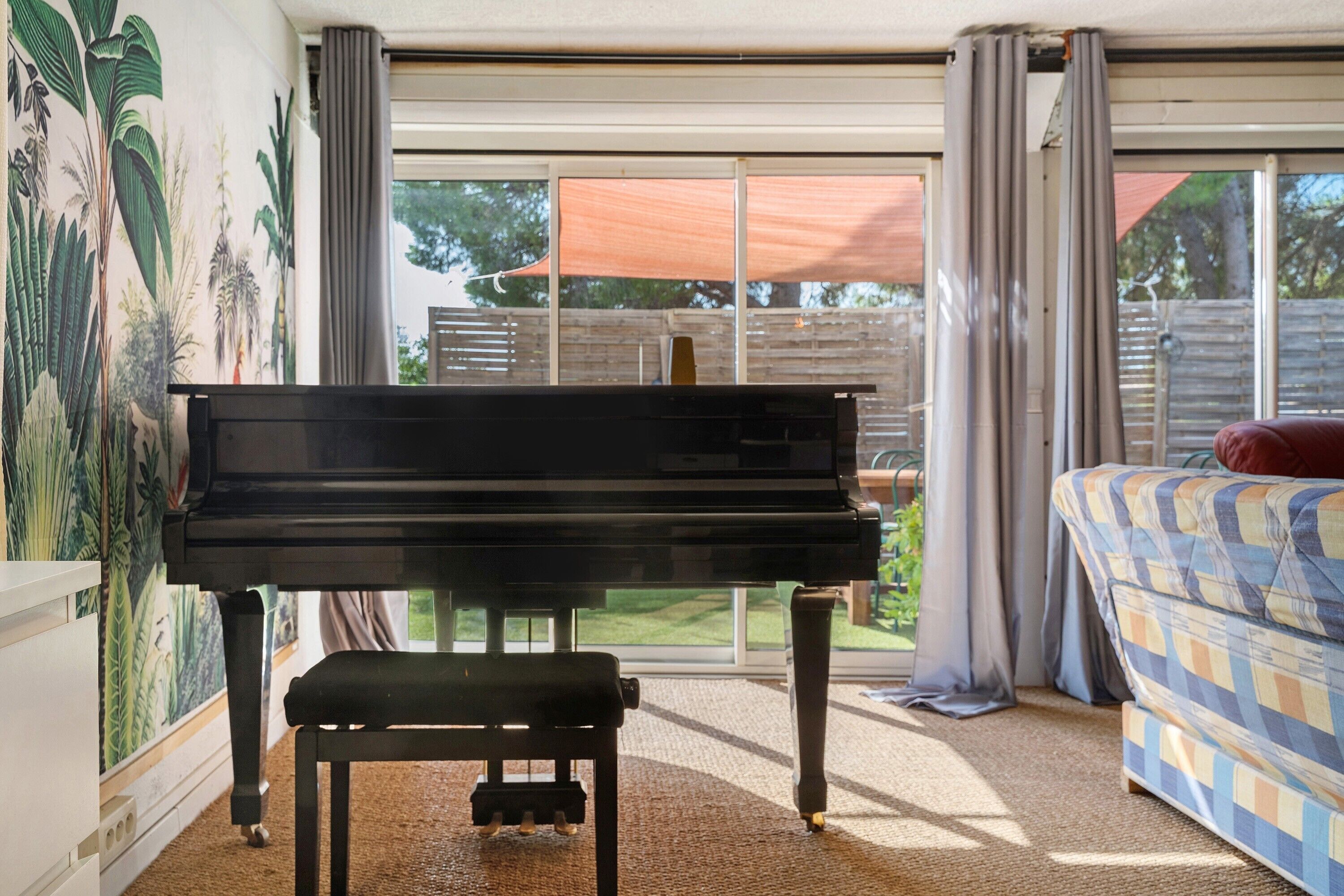A room with a piano, a couch, and a large window with a view of a backyard.