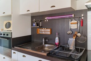 A modern kitchen with a built-in oven, a stainless steel sink, and a variety of utensils and containers on the wall. - Apartment 'Villa Andalouse' with Private Terrace, Wi-Fi and Air Conditioning (Poussan)