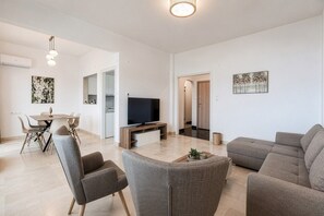 Ein modernes Wohnzimmer mit Flachbildfernseher, grauen Sofas und einem Essbereich mit Tisch und Stühlen.