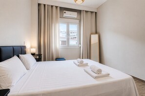 A hotel room with a bed, a nightstand, a lamp, a window with curtains, and an air conditioning unit. - Phos Residence by Rentals Pro - Neos Marmaras Halkidiki (Neos Marmaras)
