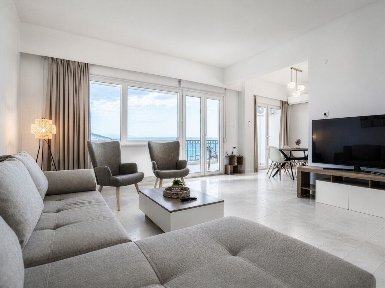 Un salon moderne comprenant un canapé, des fauteuils, une table basse, un téléviseur et un balcon avec vue.