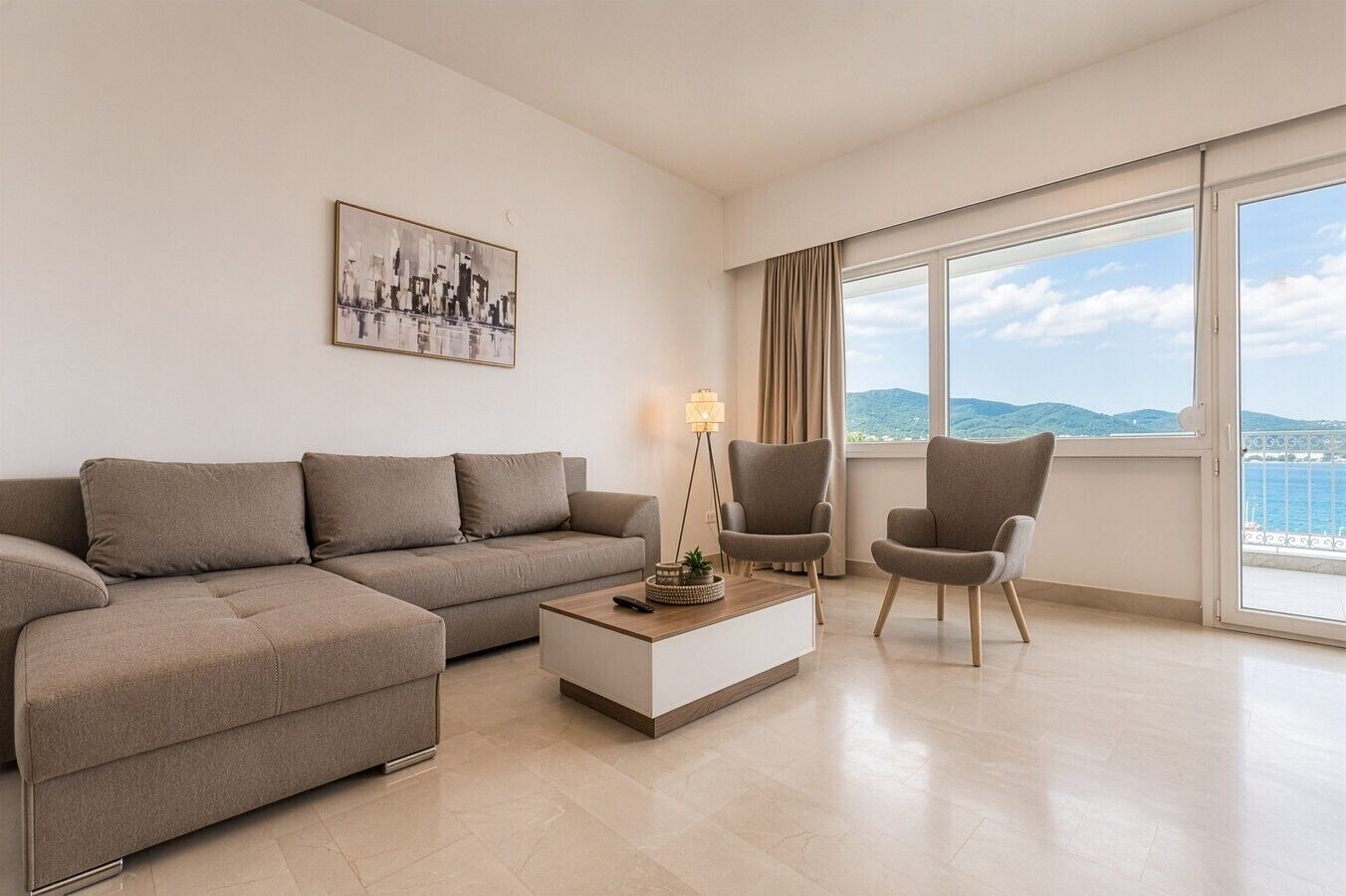A modern living room with a sofa, two armchairs, a coffee table, and a large window with a view of the sea.