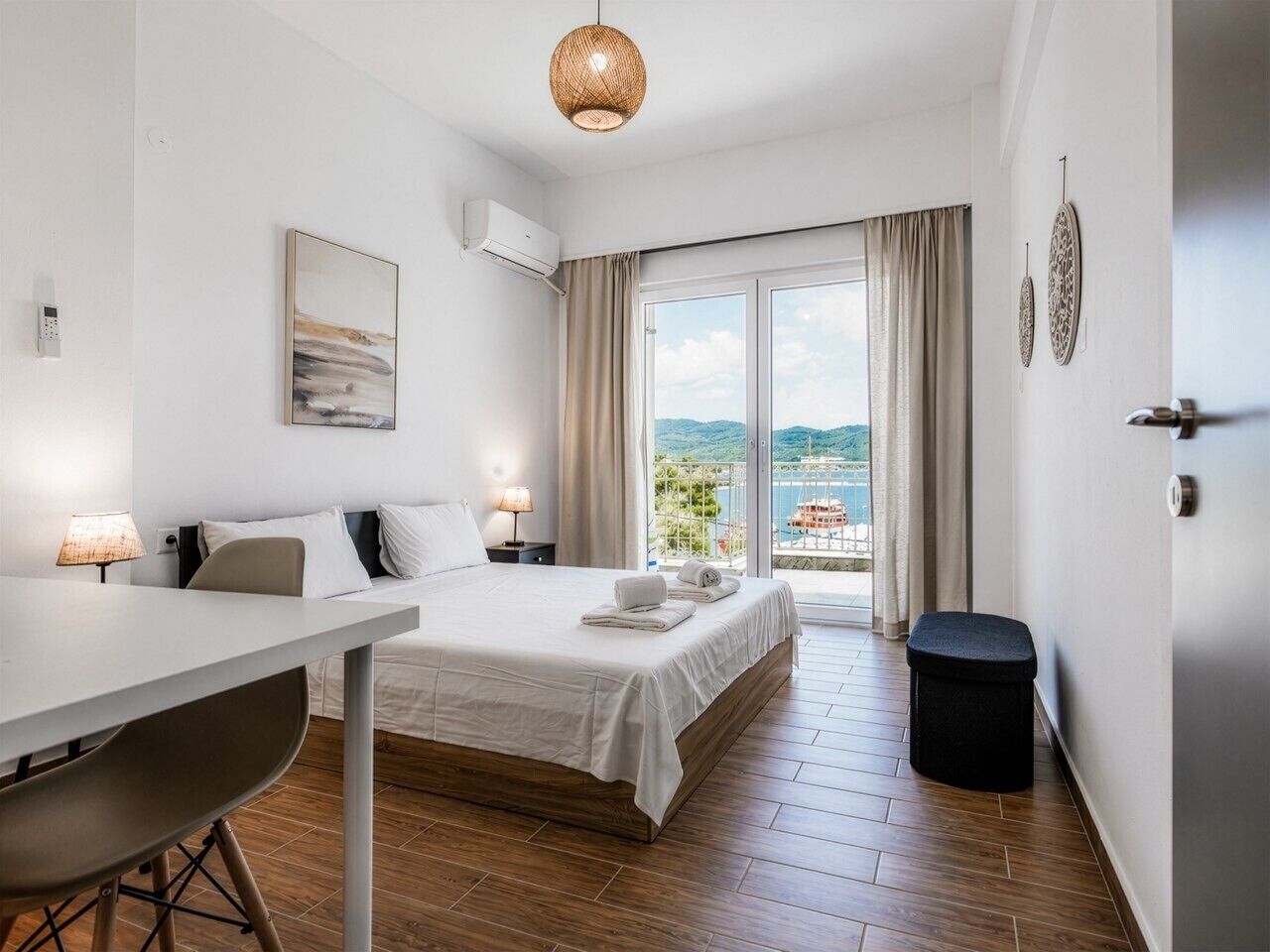 Ein Hotelzimmer mit Bett, Schreibtisch, Stuhl, Mülleimer und Meerblick durch ein großes Fenster.