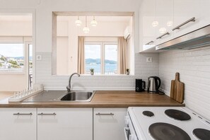 A modern kitchen with a stainless steel sink, white cabinets, a stove, and a view of the sea through large windows. - Phos Residence by Rentals Pro - Neos Marmaras Halkidiki (Neos Marmaras)