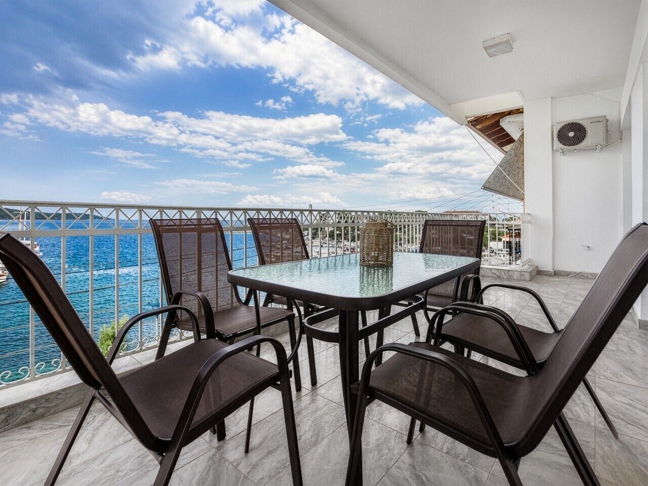 A terrace with a glass table and chairs, overlooking a body of water.