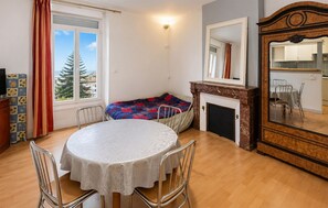 Ein Zimmer mit rundem Tisch, Stühlen, einer Couch, einem Kamin, einem Spiegel und einem fenster mit Vorhängen.