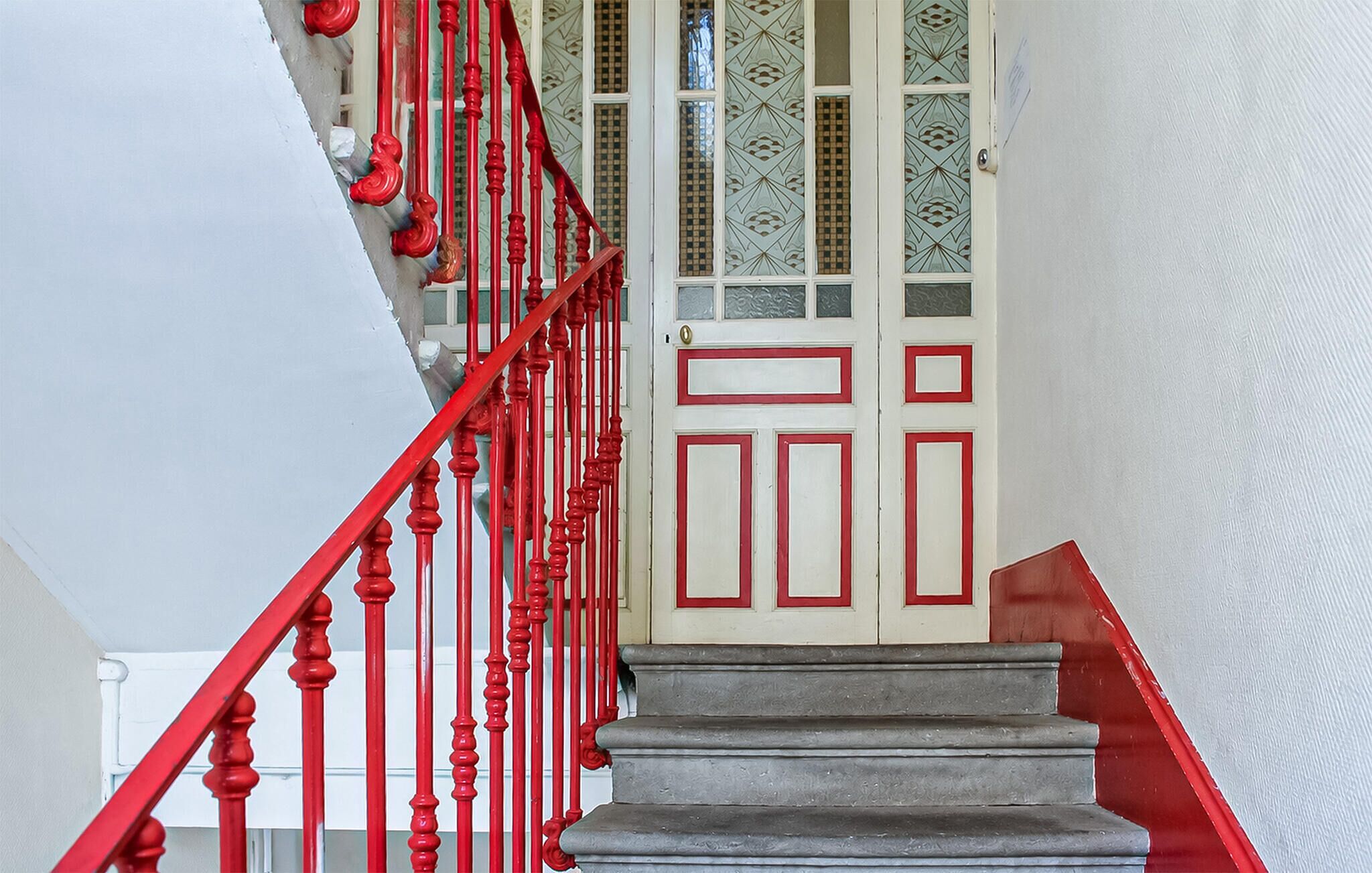 Un escalier avec des balustrades rouges menant à une porte blanche ornée d’un cadre rouge.