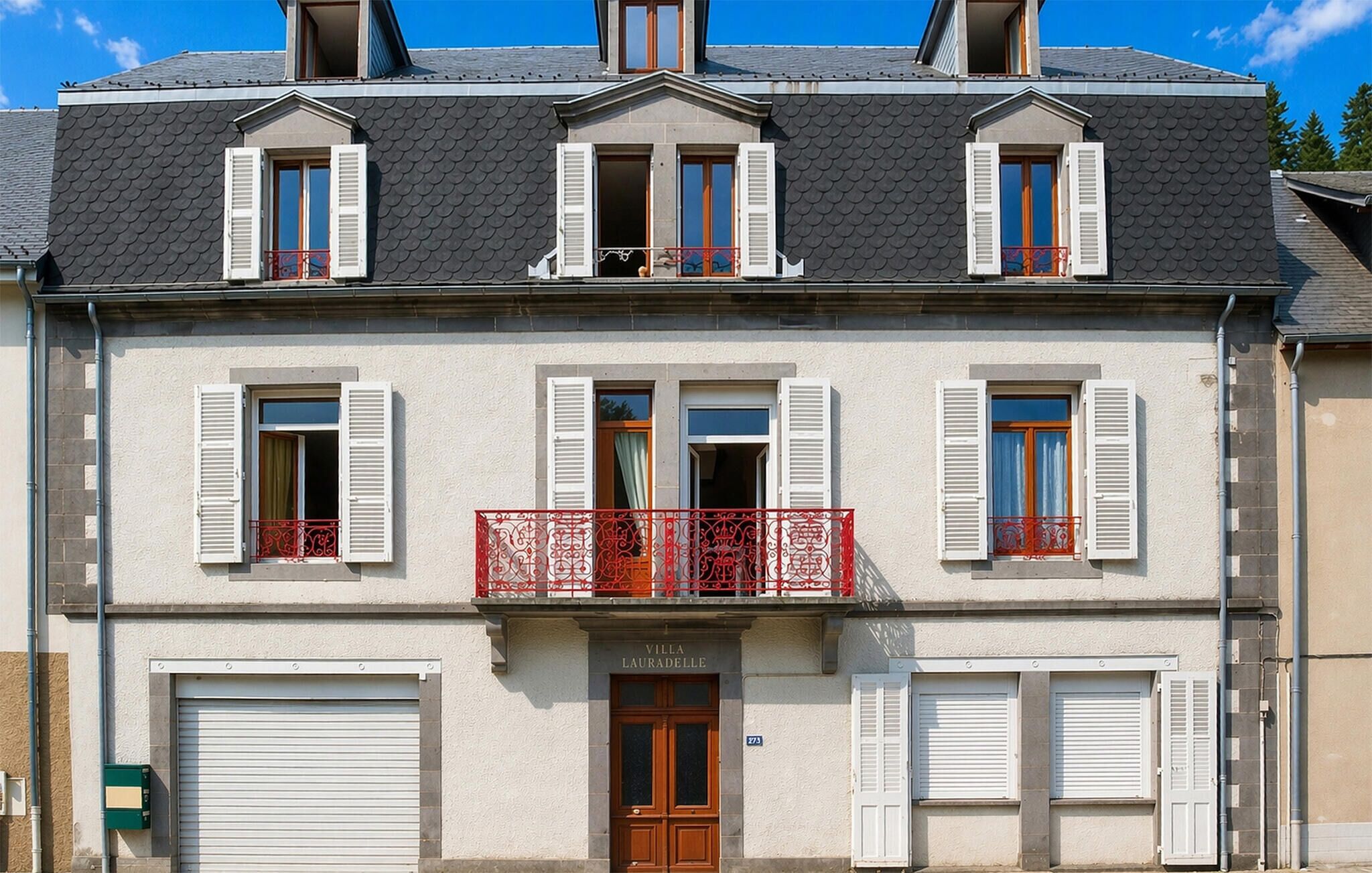 A two-story building with a balcony, shutters, and a garage door.