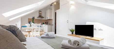 A modern bedroom with a bed, a TV, and a view of the kitchen.