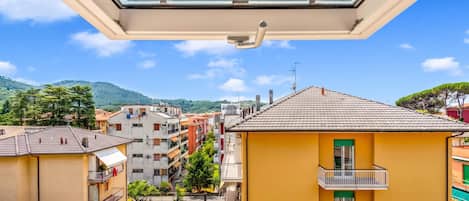 A residential building with a balcony, a view of a hillside, and neighboring buildings.