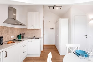 A modern kitchen with white cabinets, a stainless steel range hood, a tiled backsplash, and a wooden floor. - Central Loft Sestri Levante (Sestri Levante)
