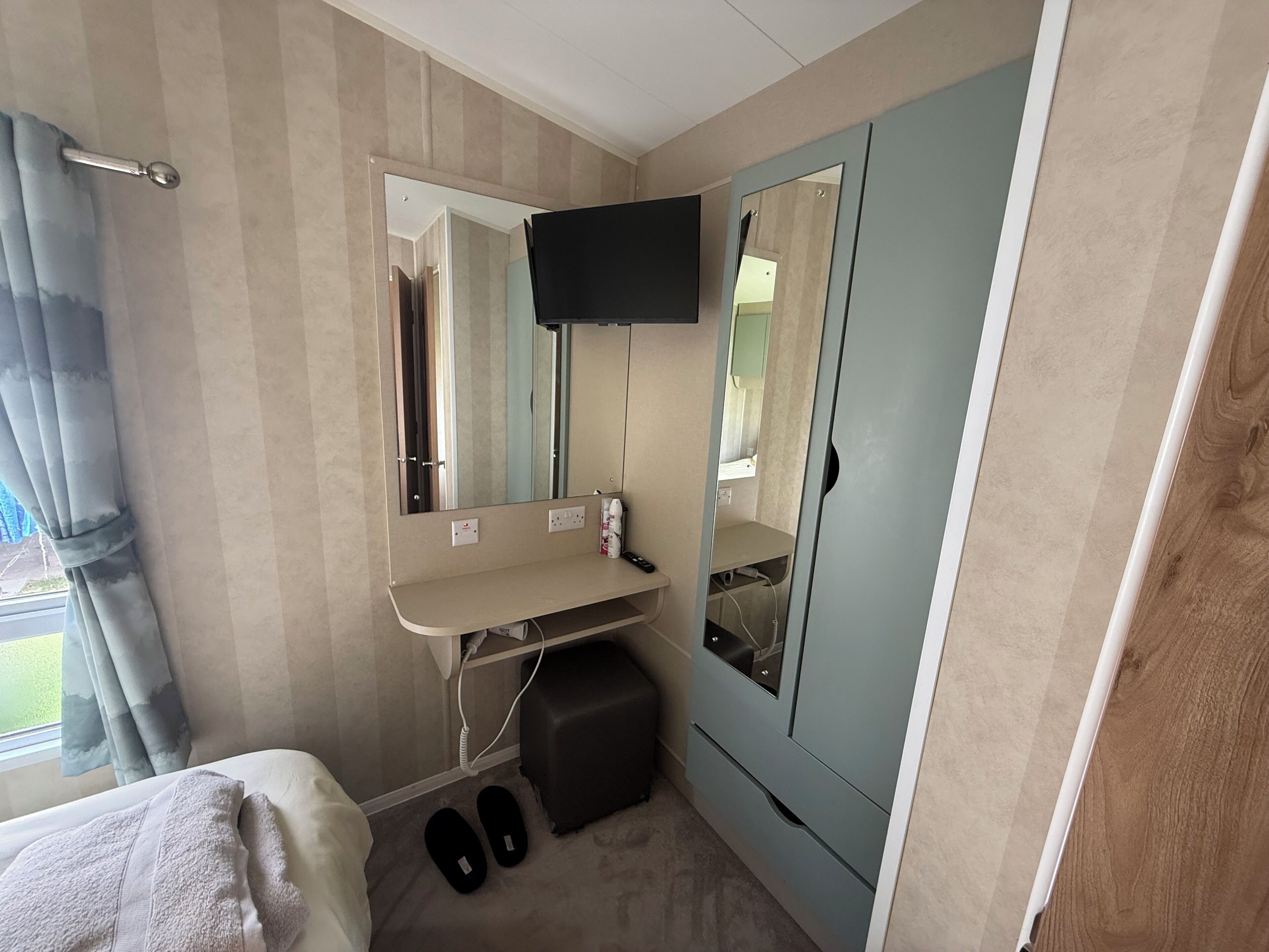 A hotel room with a bed, a small bedside table, a mirror, a TV mounted on the wall, and a wardrobe with a mirror.