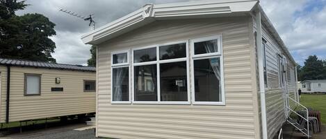 A mobile home with a large window, a satellite dish, and a small porch area.
