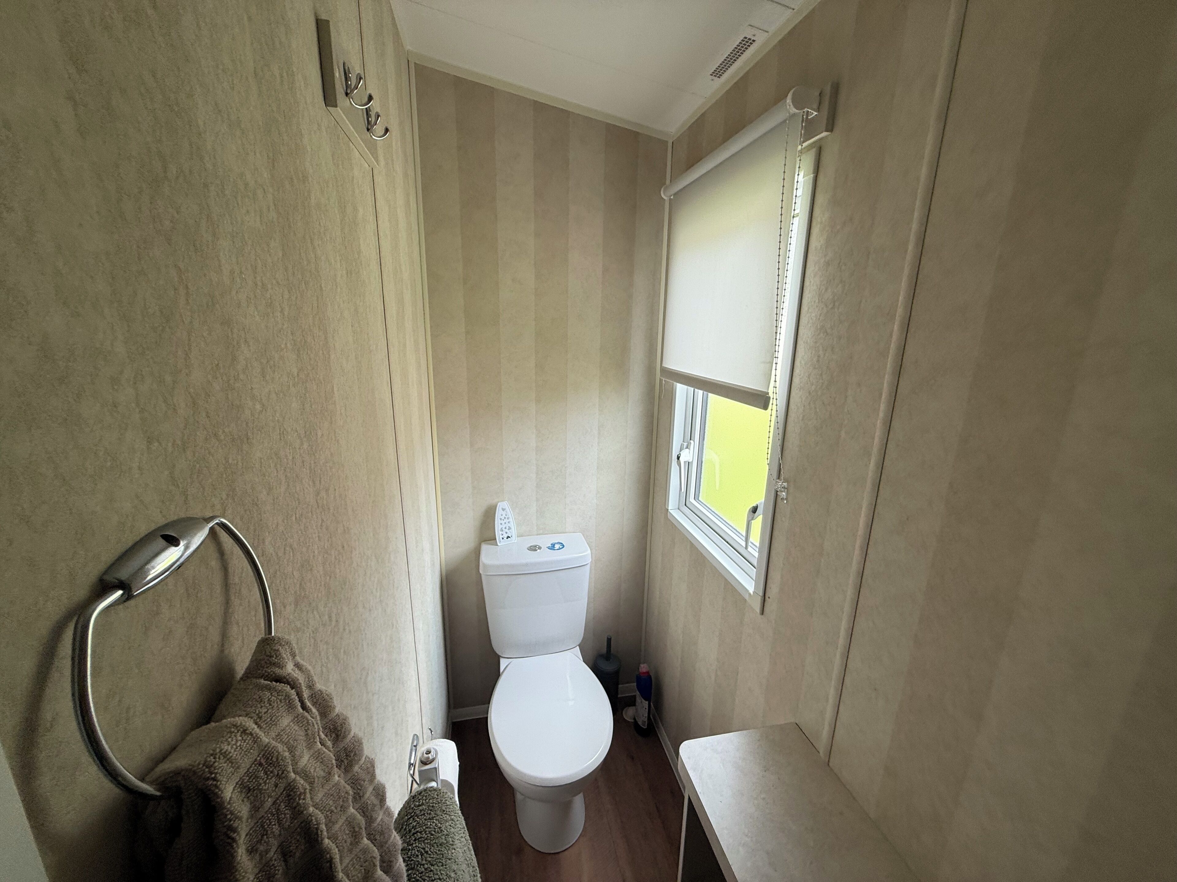 A compact bathroom with a toilet, a towel rack, and a window.
