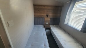 A small, narrow room with two single beds, a wooden headboard, a small table, and a window with blinds. - 2-bedroom seaside condo with mods and cons (Prestatyn)