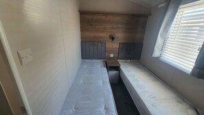 A small, narrow room with two single beds, a wooden headboard, a small table, and a window with blinds. - 2-bedroom seaside condo with mods and cons (Prestatyn)