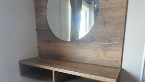 A room with a wooden vanity, a round mirror, and a small stool. - 2-bedroom seaside condo with mods and cons (Prestatyn)