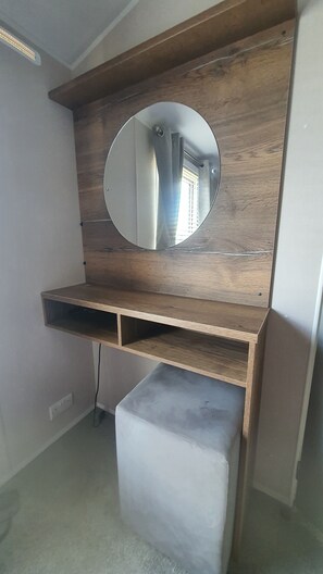 A room with a wooden vanity, a round mirror, and a small stool. - 2-bedroom seaside condo with mods and cons (Prestatyn)