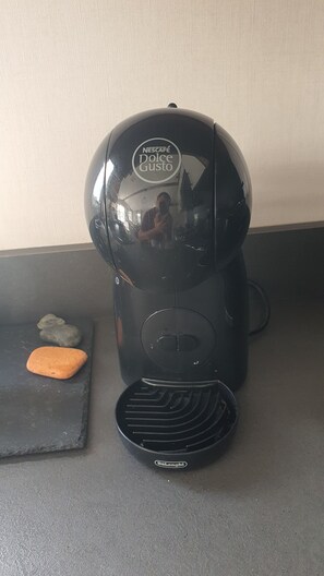 A black coffee machine with a brand logo on the top, placed on a dark countertop next to a small orange stone. - 2-bedroom seaside condo with mods and cons (Prestatyn)
