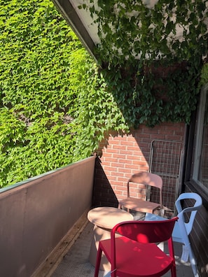 Ein Balkon mit einem roten Stuhl, einem weißen Stuhl und einem kleinen Tisch.