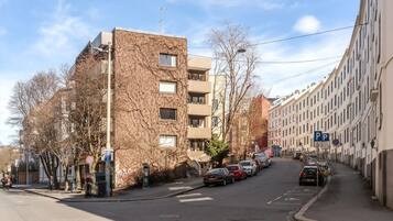 Una calle con coches aparcados, un edificio de ladrillo y una hilera de edificios blancos a la derecha.