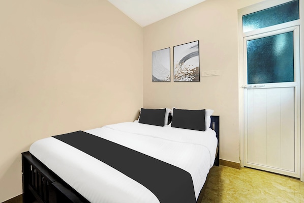 Une chambre à coucher comprenant un lit, deux oreillers, une table de chevet, une lampe fixée au mur et une porte dotée d’une fenêtre en verre dépoli.