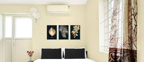 Una habitación de hotel con cama, una ventana con cortinas, un equipo de aire acondicionado y decoración en la pared.