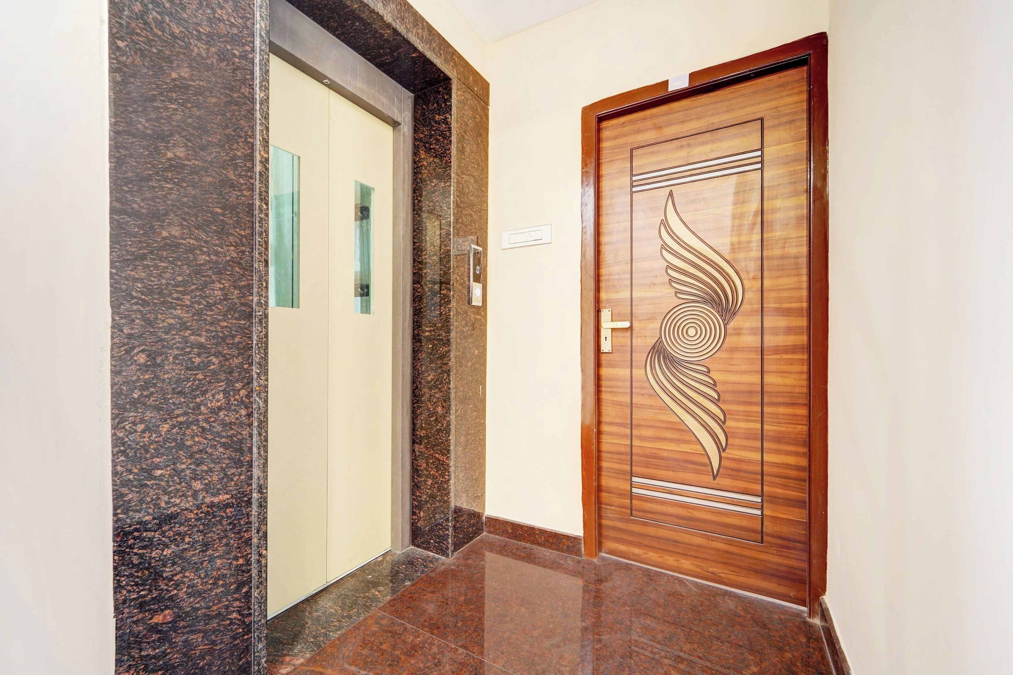 Un pasillo con piso de mármol, una puerta de madera con diseño decorativo y una pared de color claro.